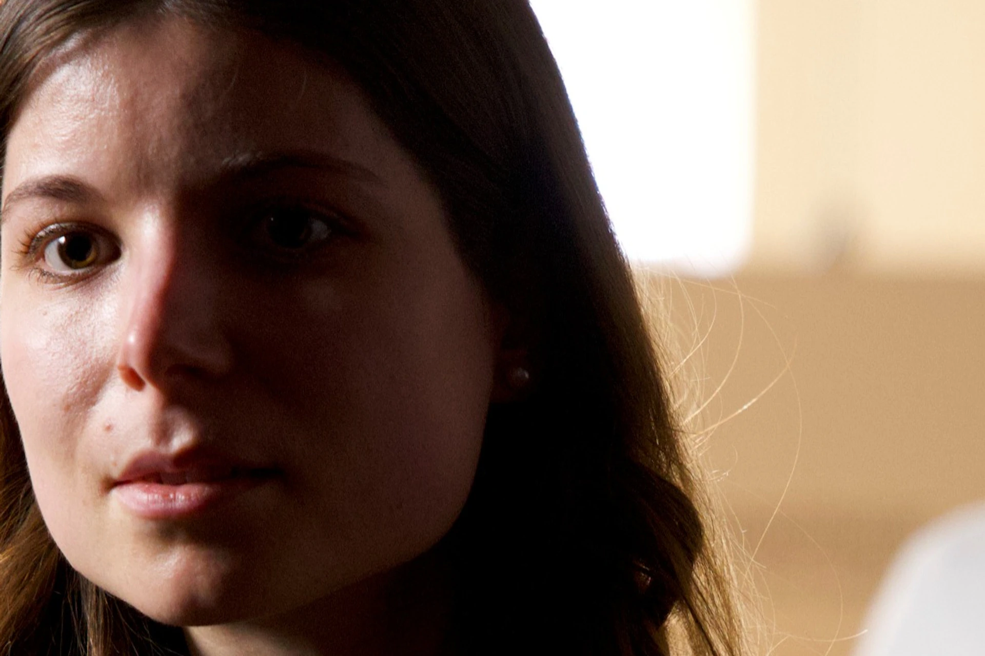 A woman looks eagerly behind a curtain into a dark room.