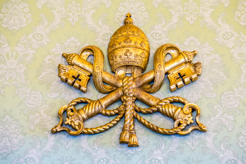 Golden papal tiara and crossed keys emblem on a pale green patterned background.