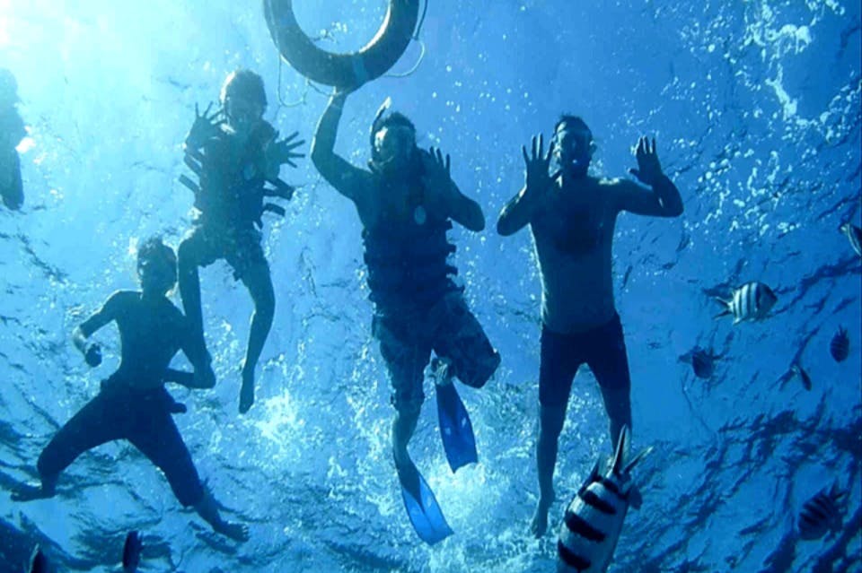 Quatre persones sota l&#39;aigua amb equip de bany, una d&#39;elles amb un anell salvavides, envoltades de peixos en aigües blaves.