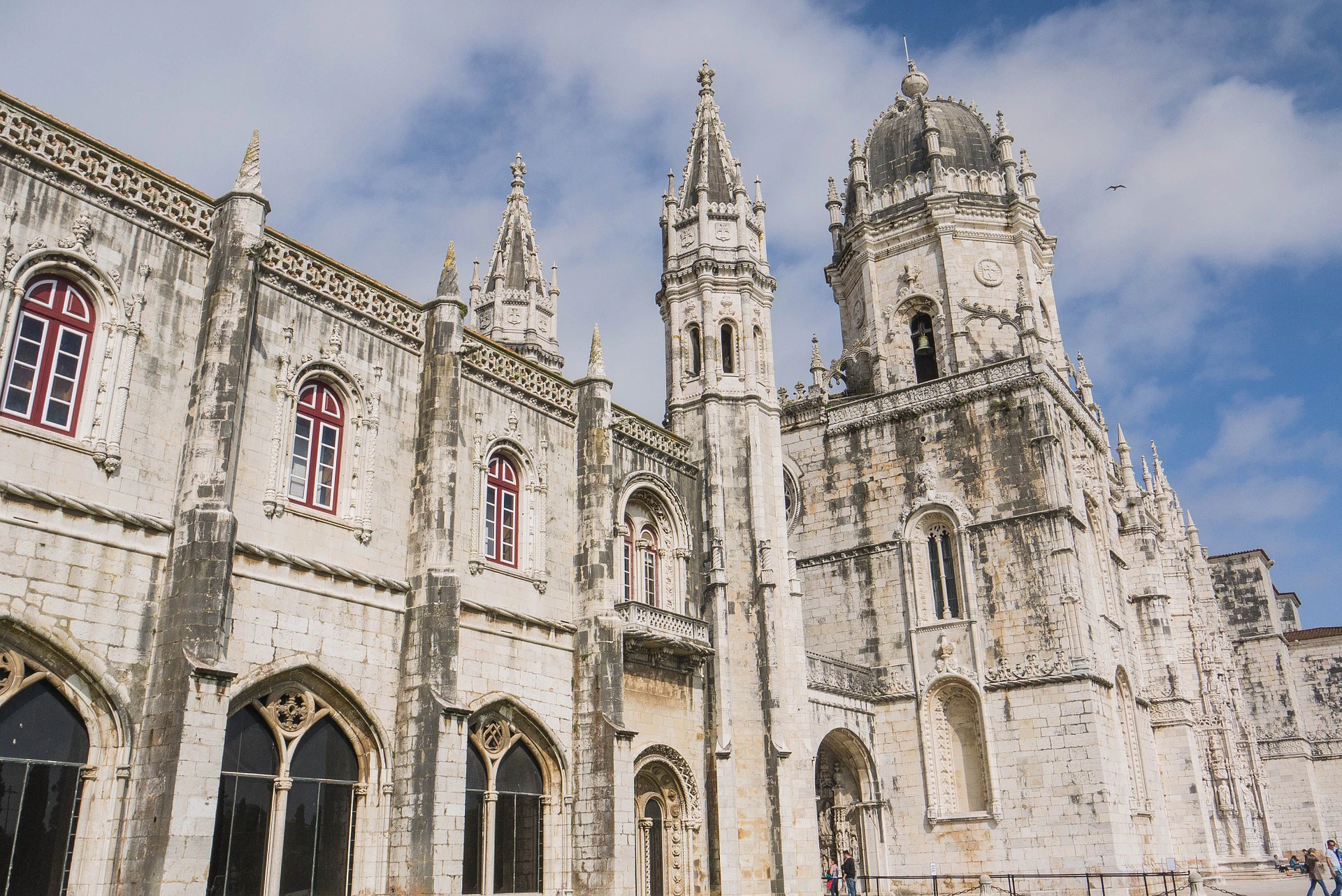 Historic stone building with gothic architecture, arched windows, ornate spires, and a clock tower under a blue sky.