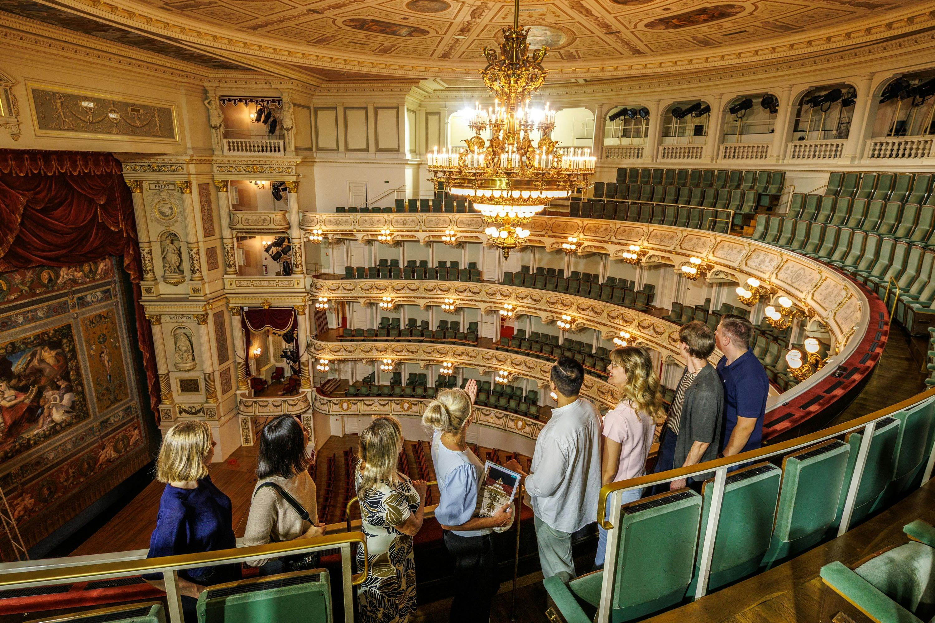 Un gruppo di persone visita un teatro sfarzoso con balconate a più livelli, dettagli decorativi e un maestoso lampadario.