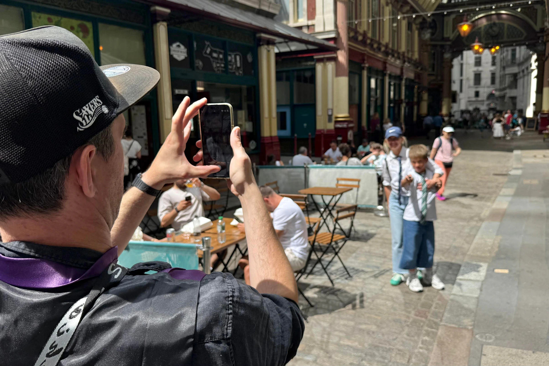 Two people posing for a photo while another person takes their picture in a lively outdoor market setting with tables and chairs.