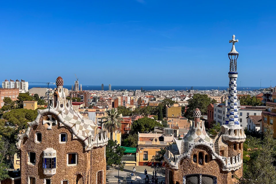 A cityscape from an elevated view, featuring unique architectural buildings in the foreground and a coastline in the distance.