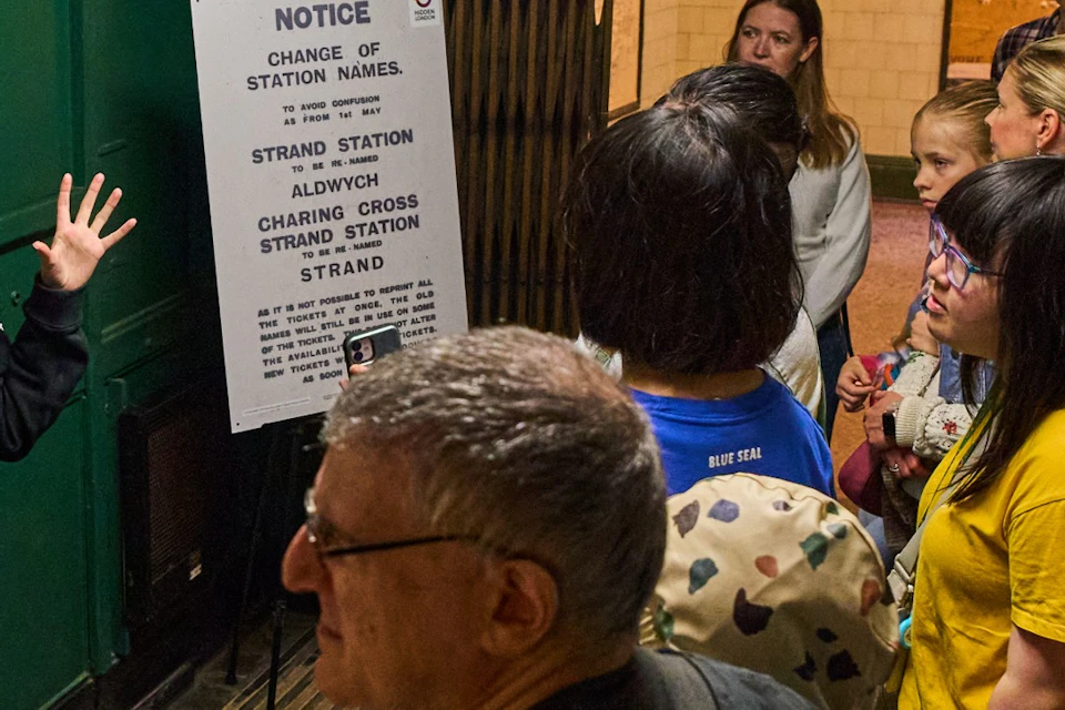 A guide speaking to a group of people in a green-walled room with informational signs and a map display.