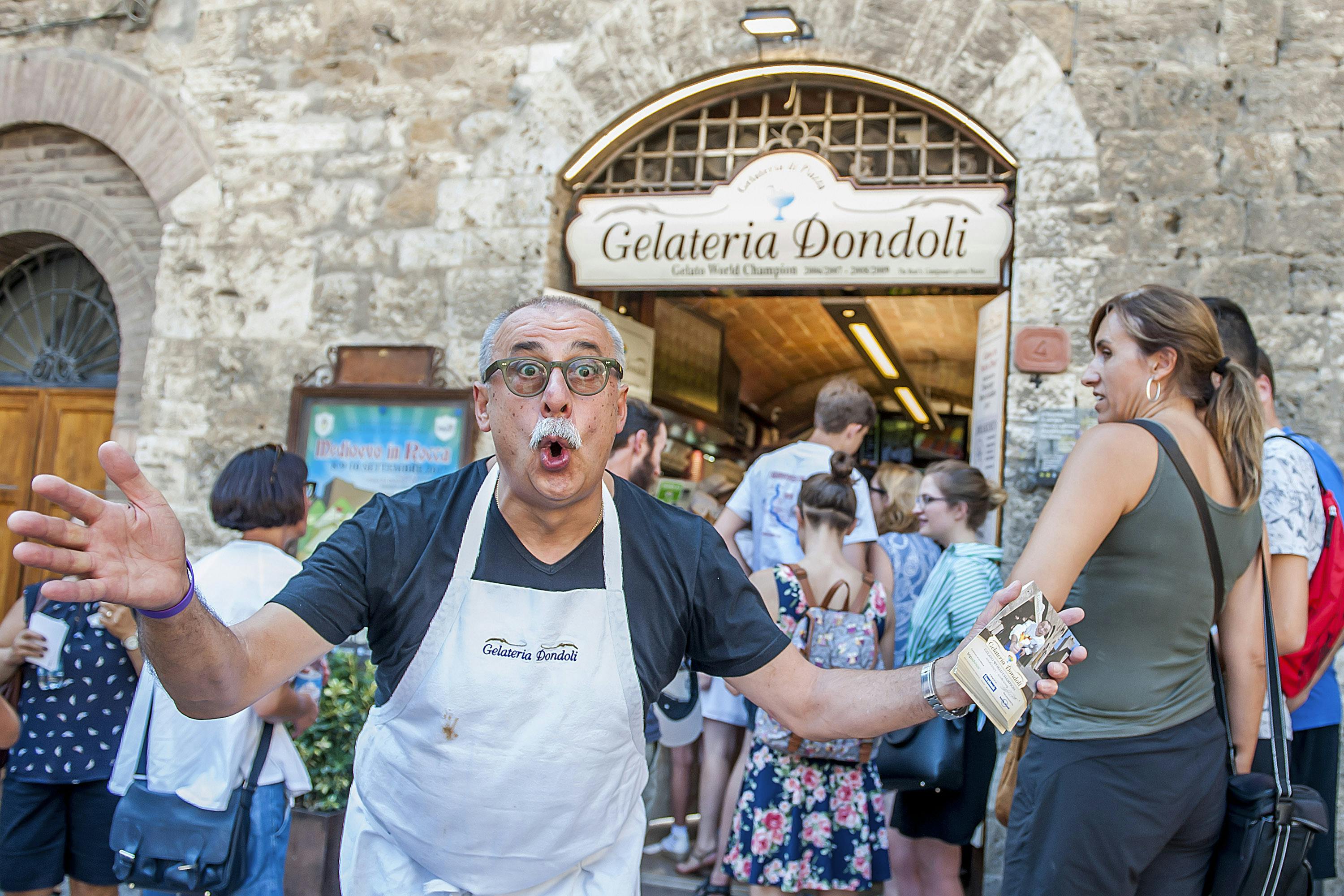 Gelateria Dondoli前面站着一位围裙的表情丰富的男士，入口附近聚集着一群人。