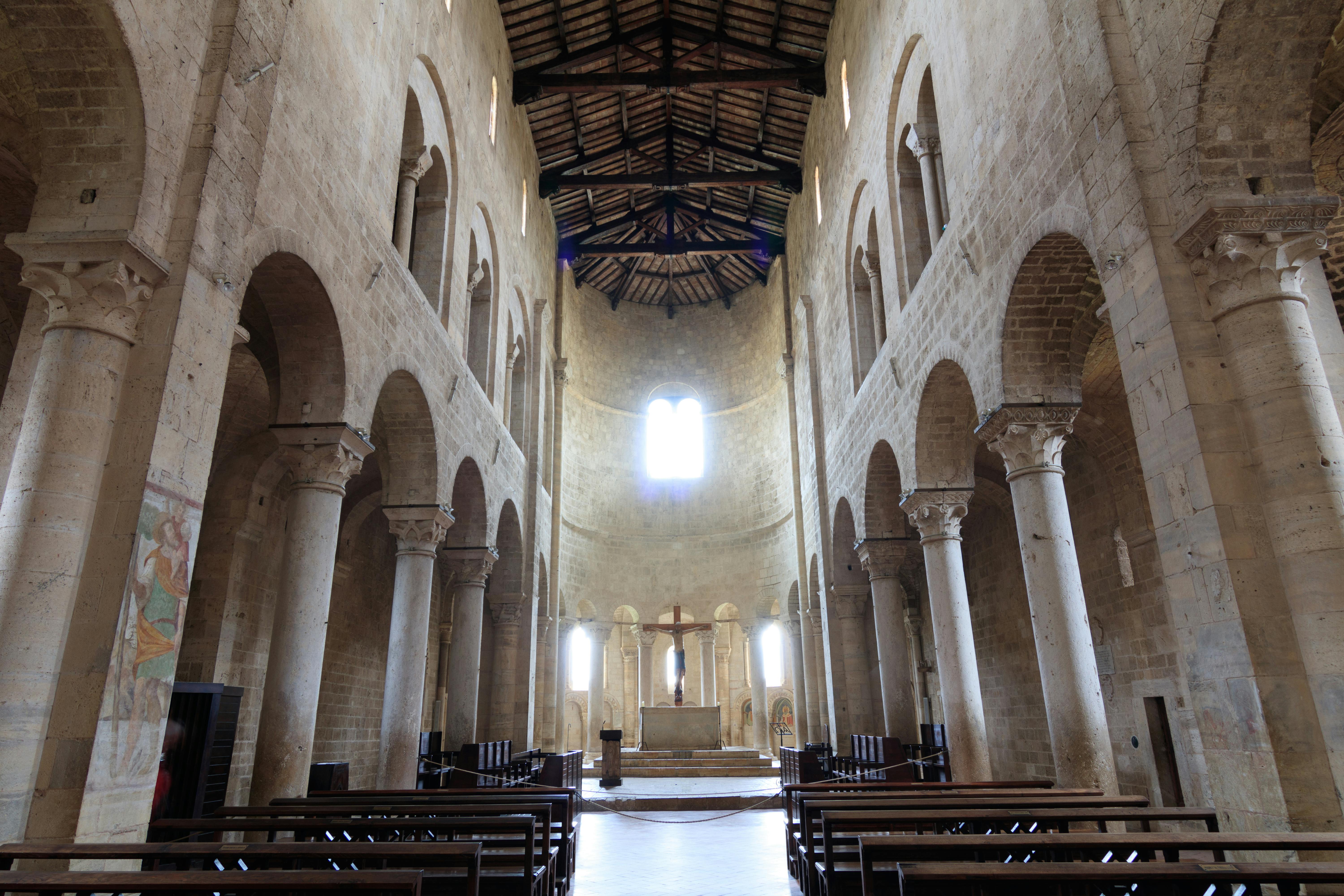 Interior of a large, empty cathedral with high vaulted ceilings, stone arches, and an altar with a cross at the far end.