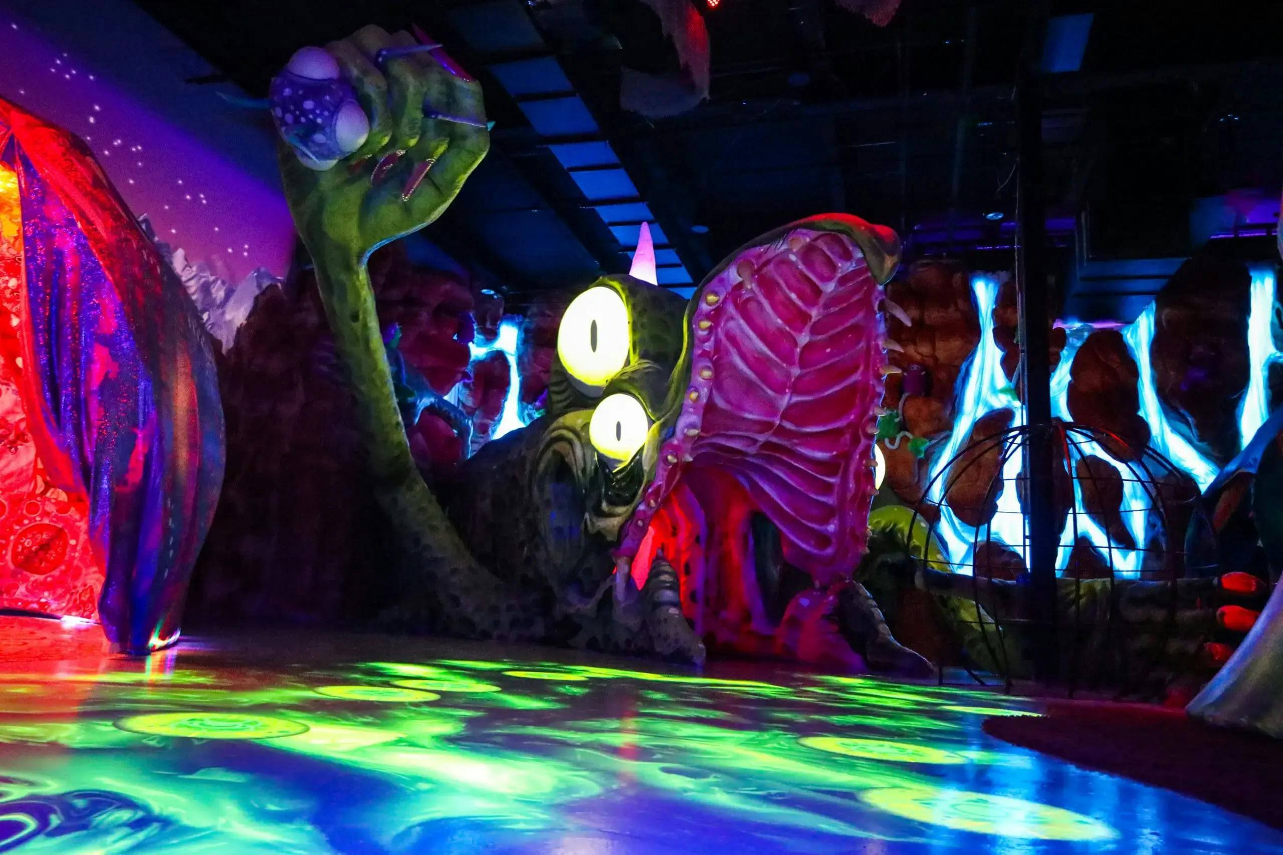 A large, fantastical creature with glowing eyes and a wide-open mouth in a dimly lit, vividly colored environment.