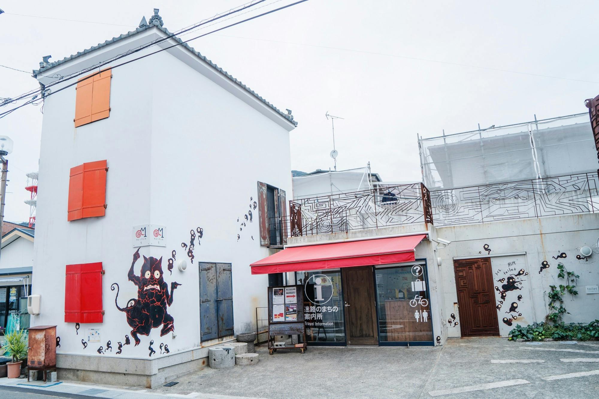 A white building with a red awning, decorated with black and red artwork, and signage for an information center.