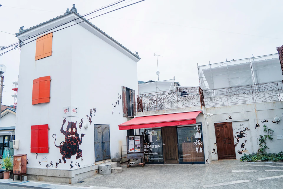 A building with an illustration of a demon on the wall, a red awning, and signs indicating an information center and bicycles.