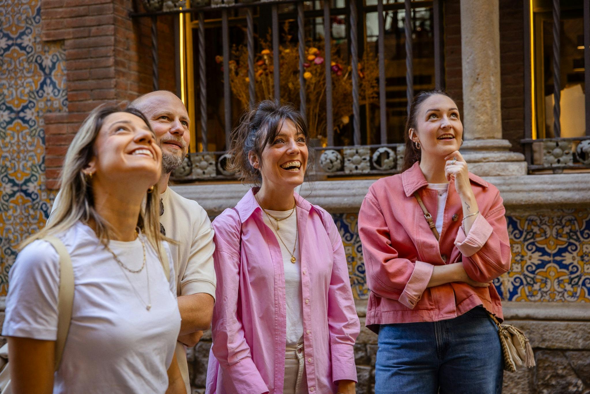 Quatre personnes se tenant ensemble en plein air, souriant et regardant vers le haut, devant un mur décoratif et une balustrade.