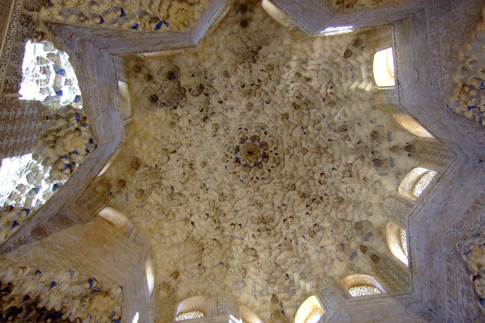 An intricately detailed ceiling with geometric patterns and small windows, featuring a central ornate design.