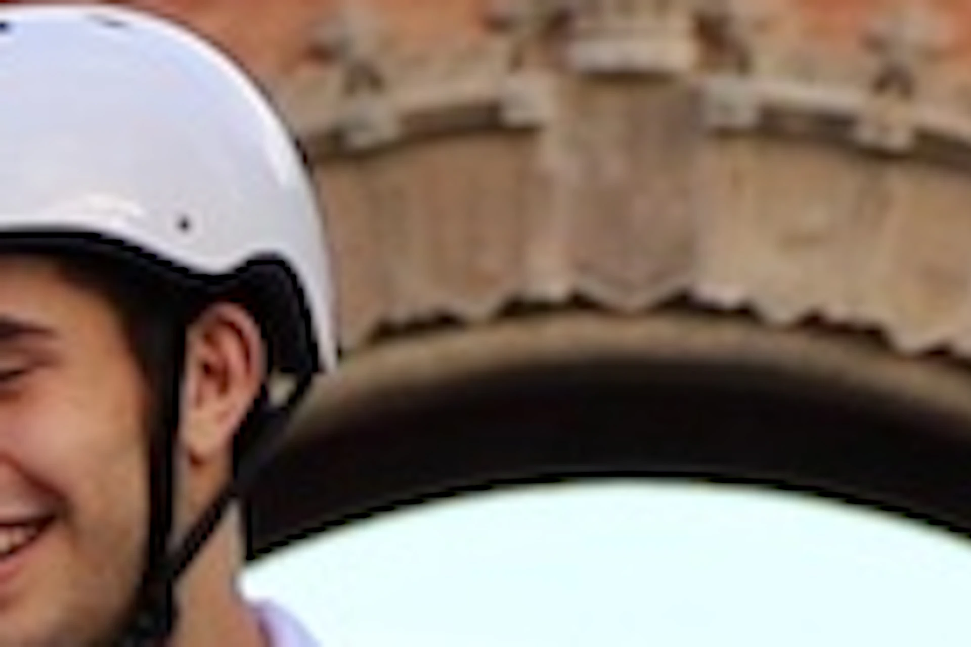 Two people wearing helmets ride Segways on a wide path with the Arc de Triomf and palm trees in the background.
