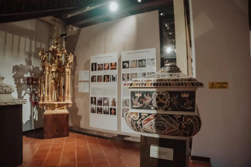 A museum exhibit showcasing an ornate urn in the foreground with a golden religious artifact and informational panels in the background.
