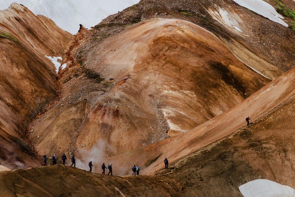Els excursionistes travessen un paisatge escarpat i estèril amb tons terrosos barrejats i taques de neu.