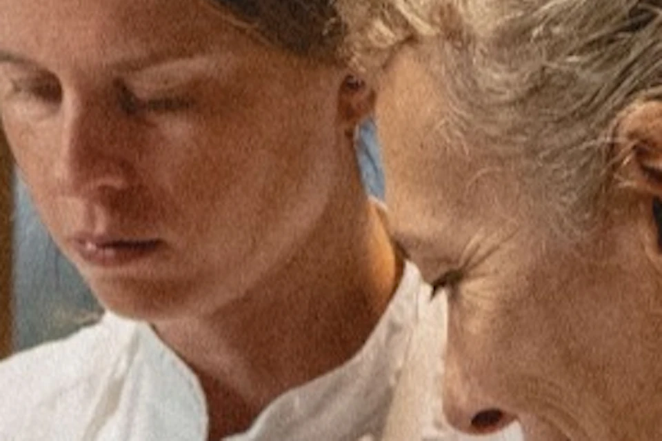 Two chefs in white uniforms cooking, one stirring a pot while the other observes.