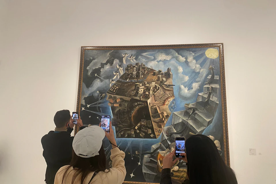 People taking photos of a surrealist painting featuring a floating landmass under a bright light in an art gallery.