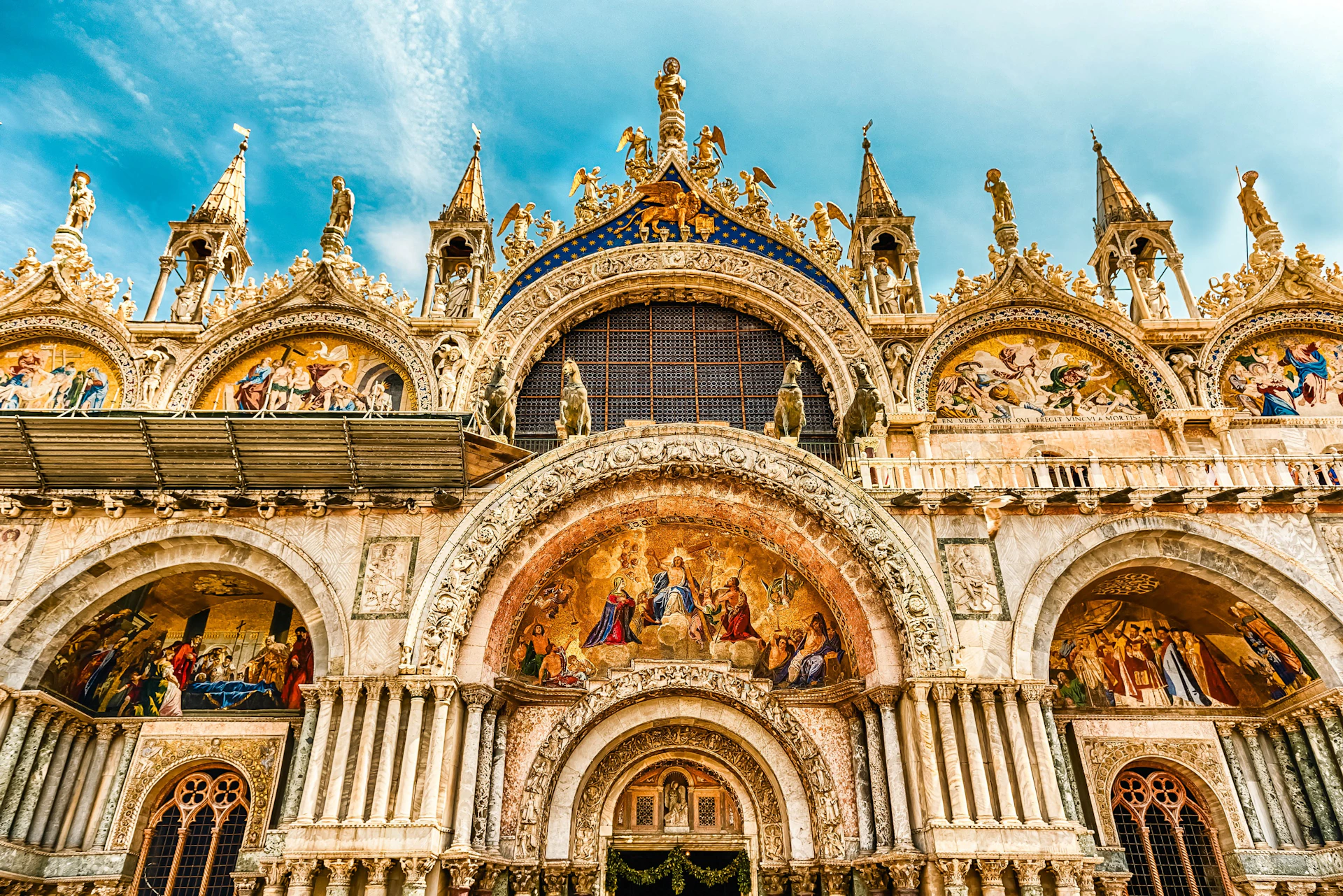 Ornate cathedral facade with intricate arches, sculptures, and religious mosaics under a blue sky.