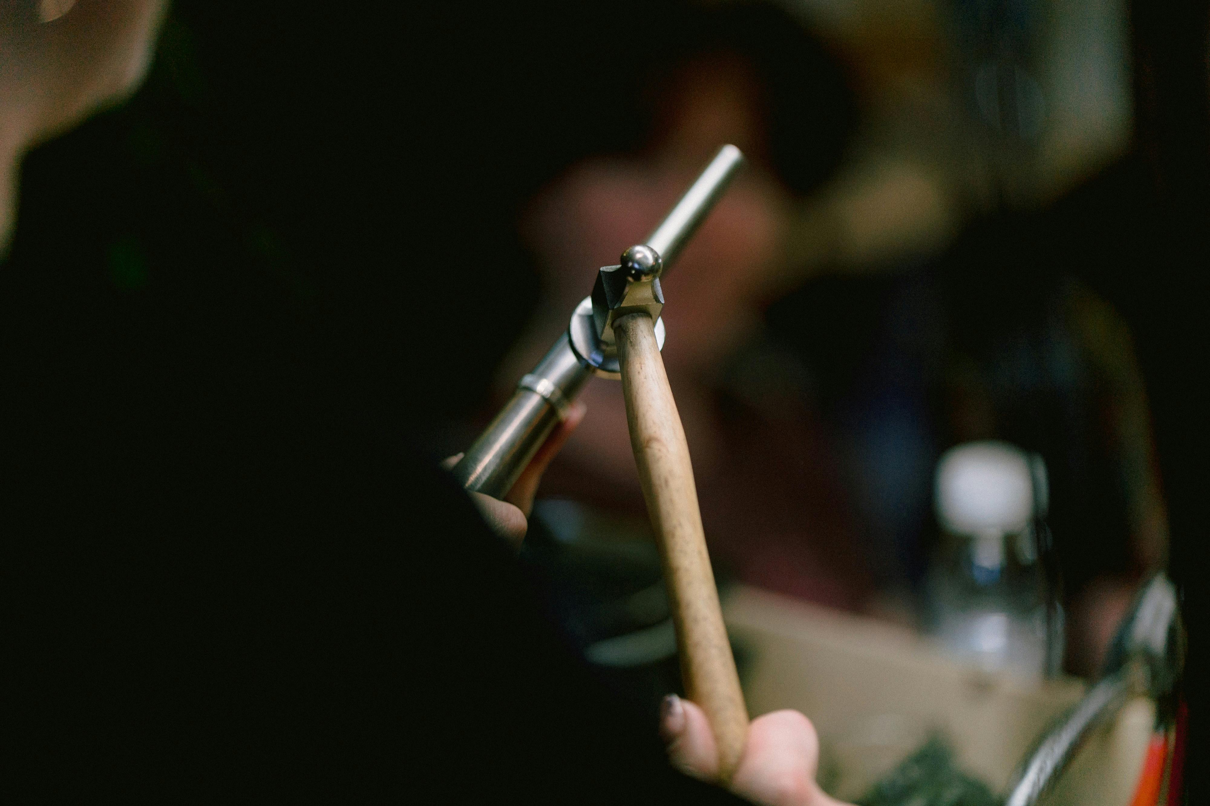 A person holds a wooden-handled tool near a device on a blurred background.