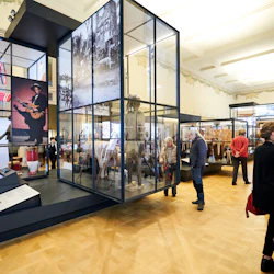 Museigalleri med människor som tittar på olika kulturella utställningar och artefakter som visas i glaslådor.