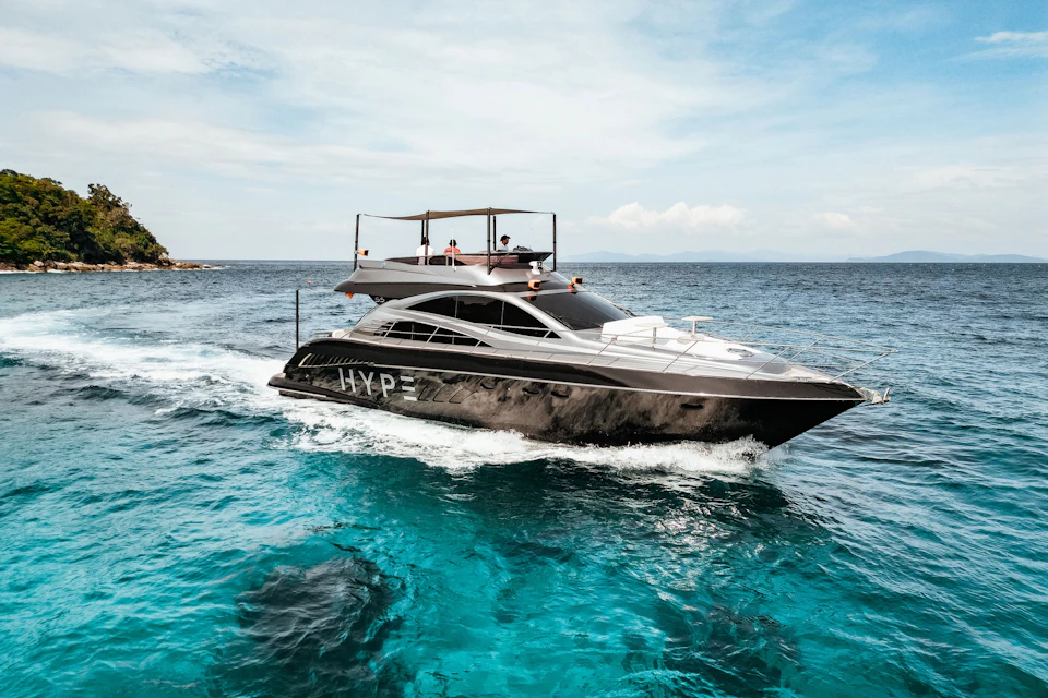 A motor yacht named "HYPE" cruising on clear blue water under a partly cloudy sky, with passengers on the upper deck.