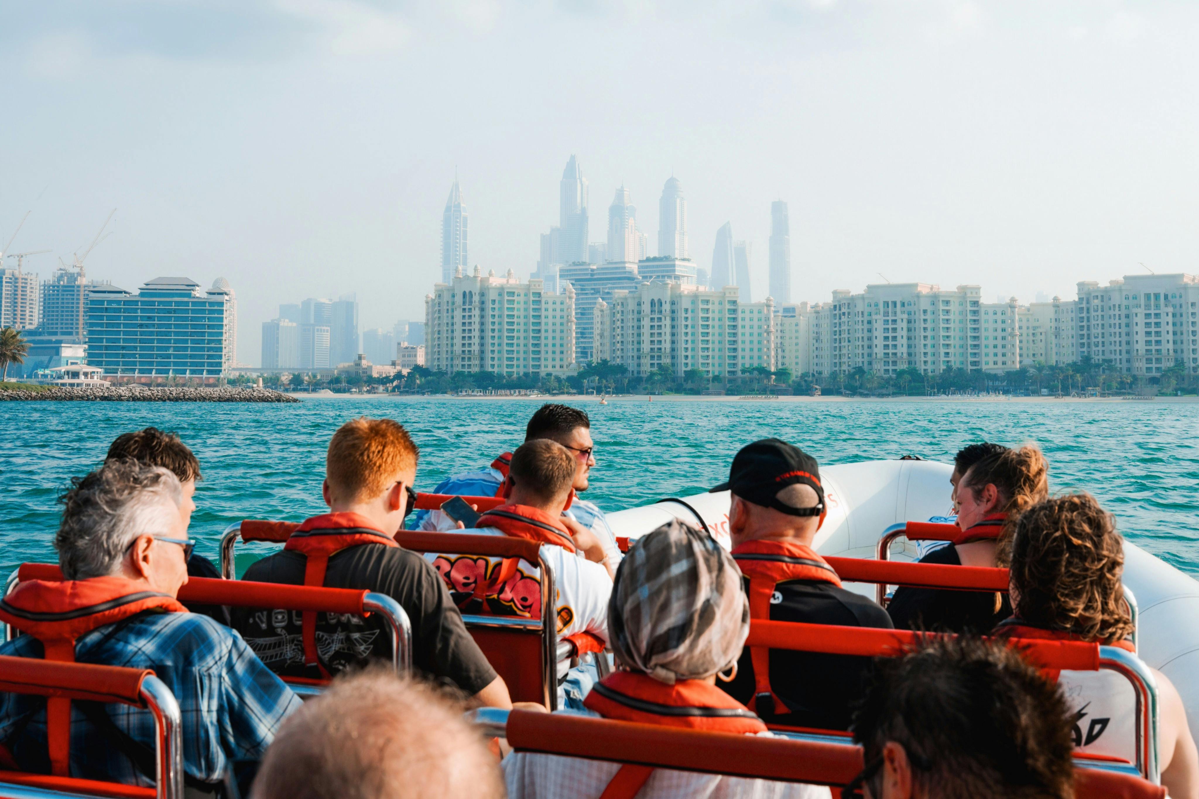 Skupina lidí v záchranných vestách na lodi s panoramatem města s vysokými budovami v pozadí.