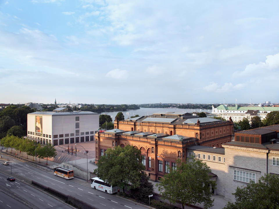 Bird's-eye view of a cityscape featuring a historic brick building, a white modern building, trees, and parked buses on a street.