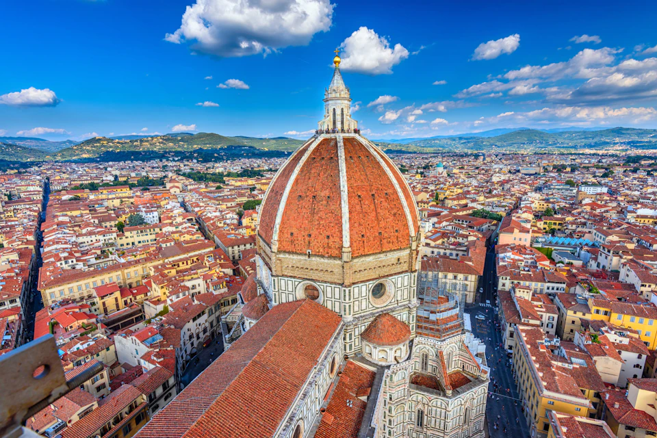 Aerial view of Florence, Italy, highlighting the large red dome of the Cathedral of Santa Maria del Fiore surrounded by buildings.