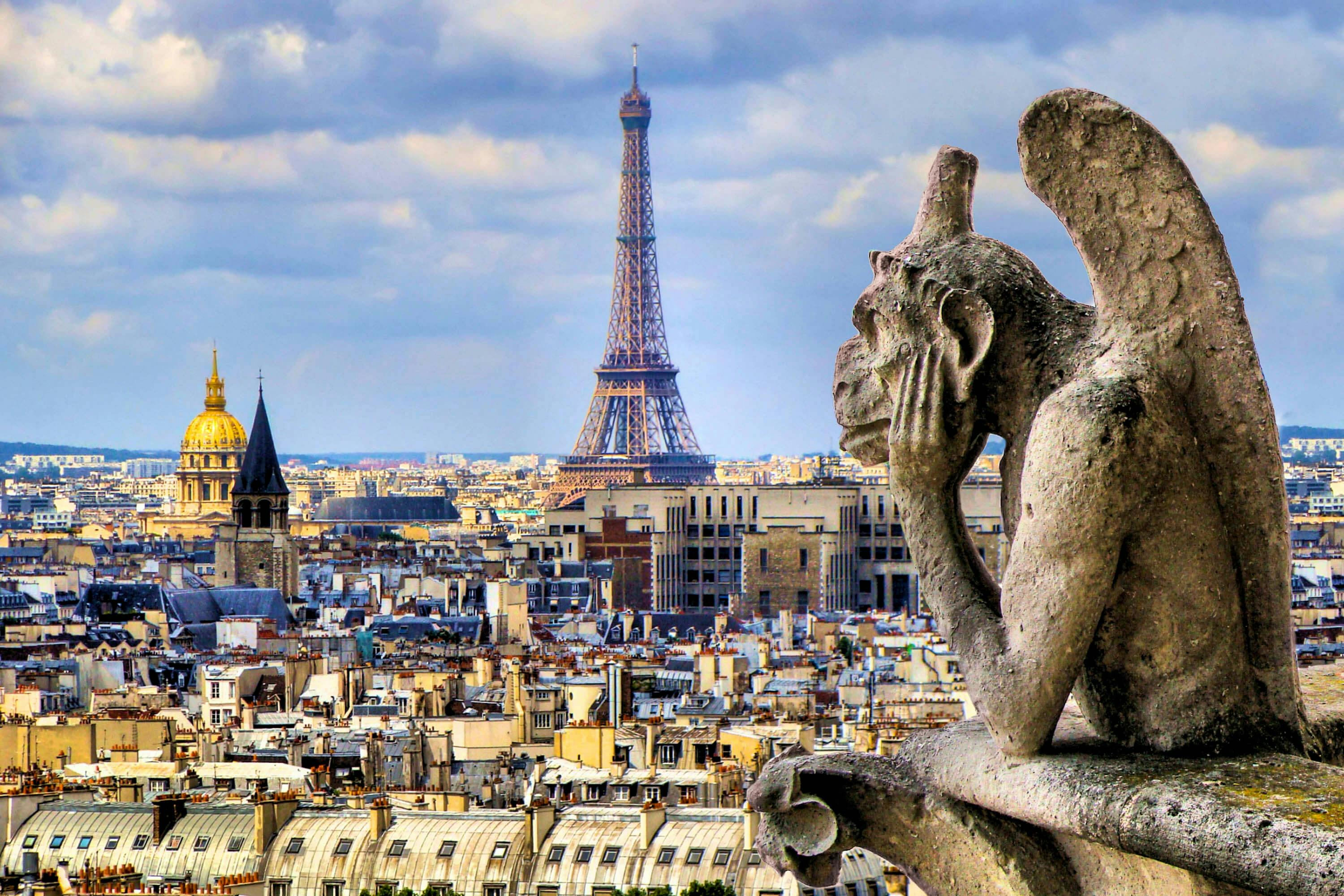 Ένα πέτρινο gargoyle βλέπει στο Παρίσι με τον Πύργο του Άιφελ να υψώνεται εμφανώς στο παρασκήνιο κάτω από έναν εν μέρει συννεφιασμένο ουρανό.