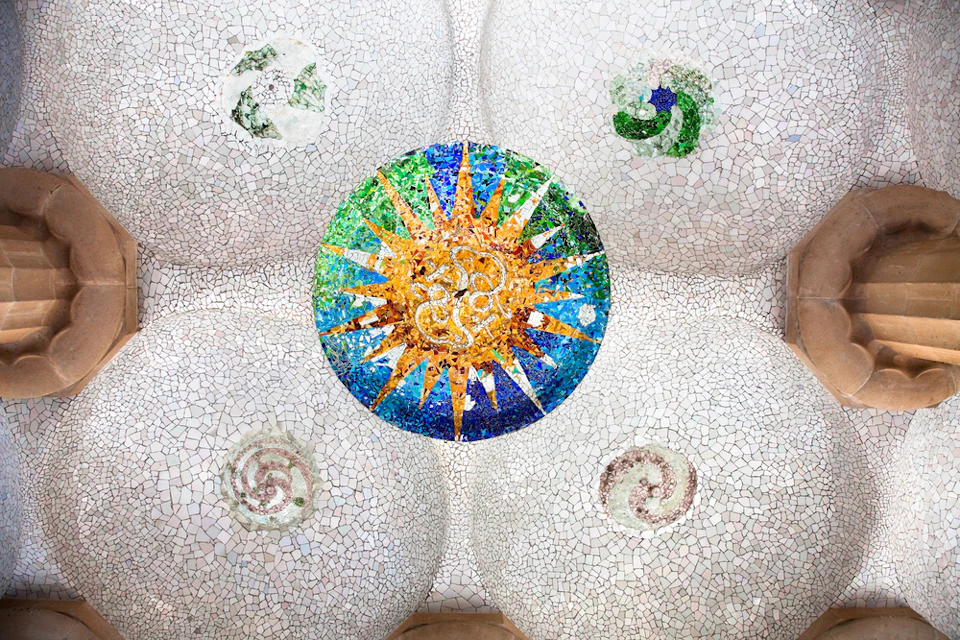 Ceiling mosaic with colorful circular sunburst pattern and spiral designs on a white tiled background, flanked by architectural details.