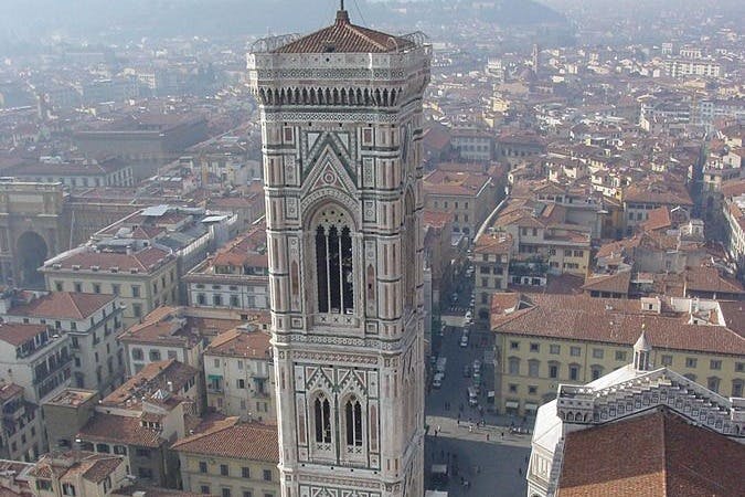 The image shows an ornate, historic cathedral with a large red-tiled dome and intricate marble facade under a clear blue sky.