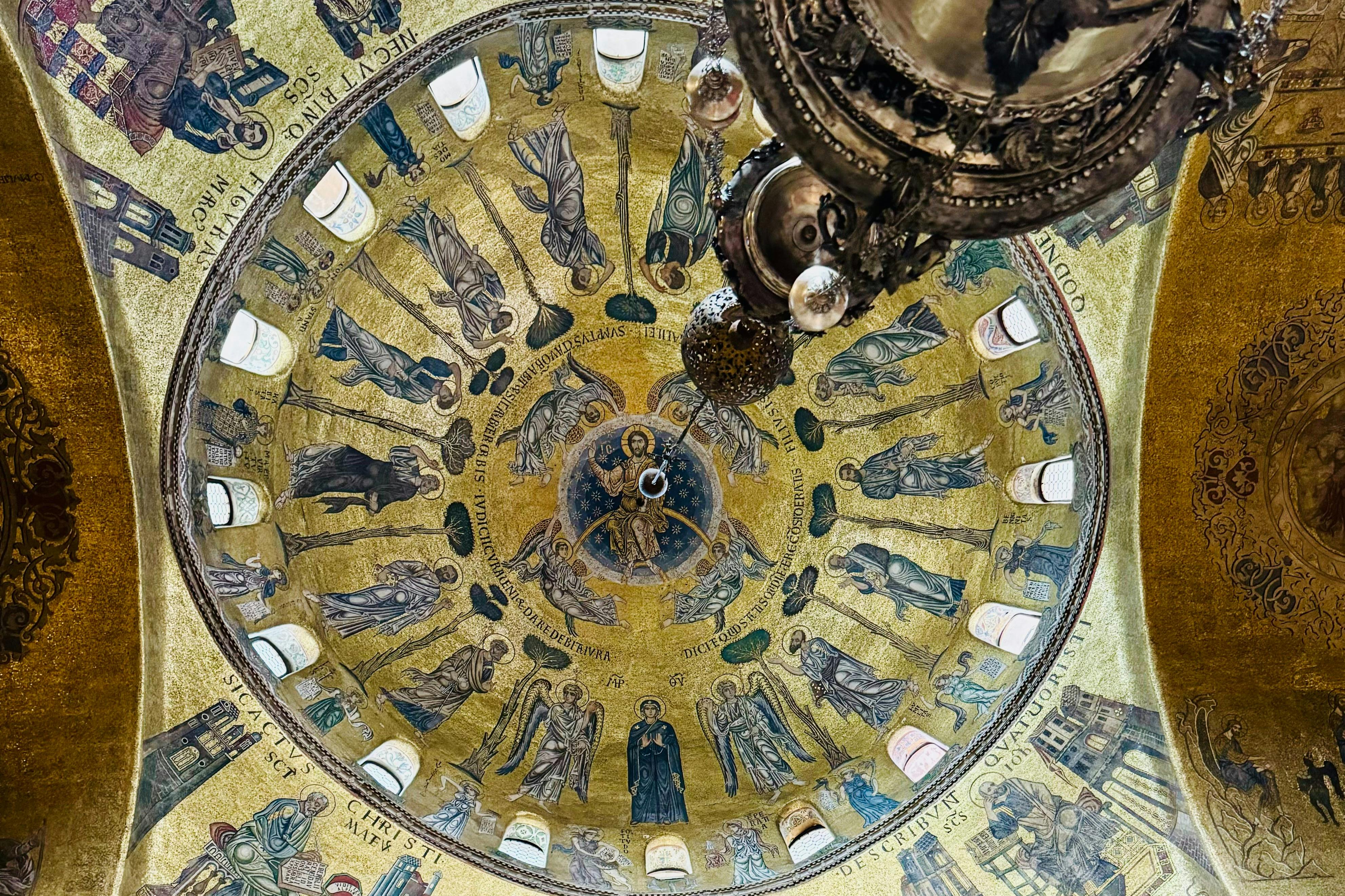 A richly decorated dome with gold mosaics and religious figures, featuring a central image of Christ, and a hanging chandelier.