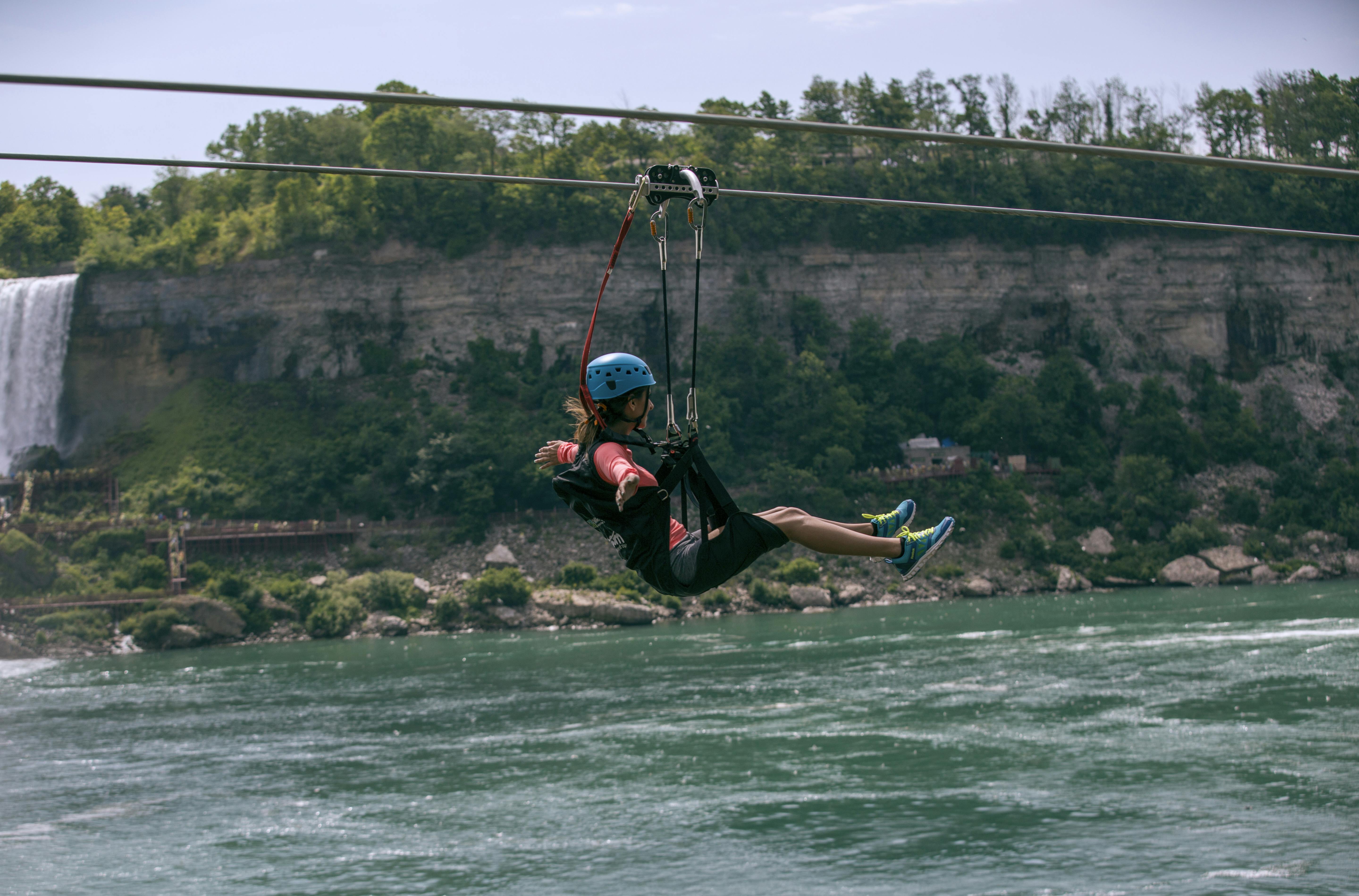 森林に覆われた崖を背景に、ヘルメットをかぶり、川にジップライニングを施した人物。