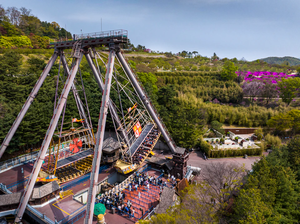 An amusement park ride shaped like a pirate ship swings on a large frame, with a queue of people waiting below.