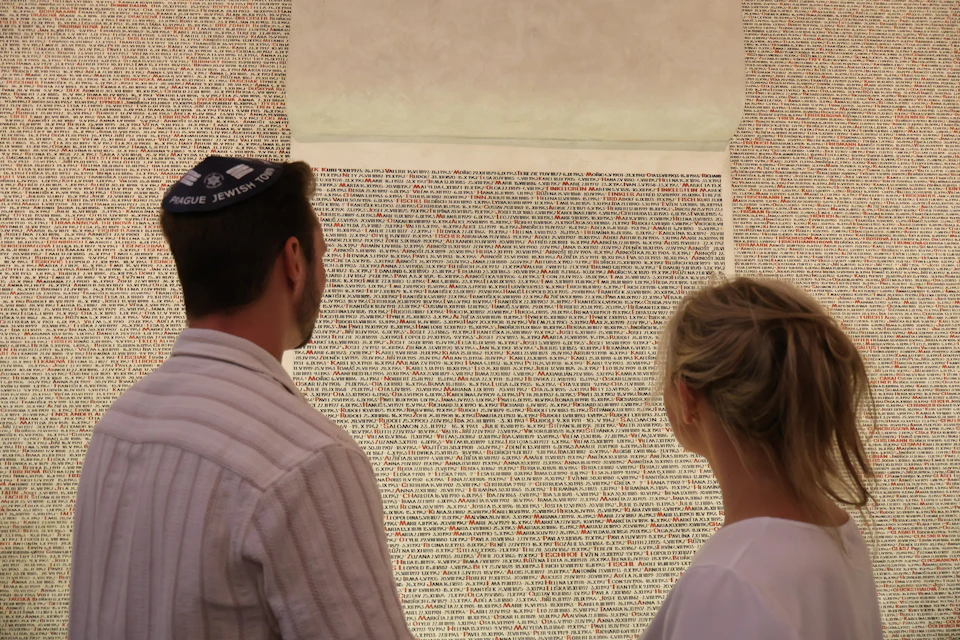 Two people are standing and looking at a wall covered in dense text, with red highlights on some words.