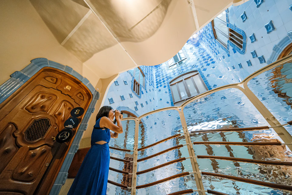 A person in a blue dress photographs the ornate blue-tiled interior of a building with curved lines and wooden details.