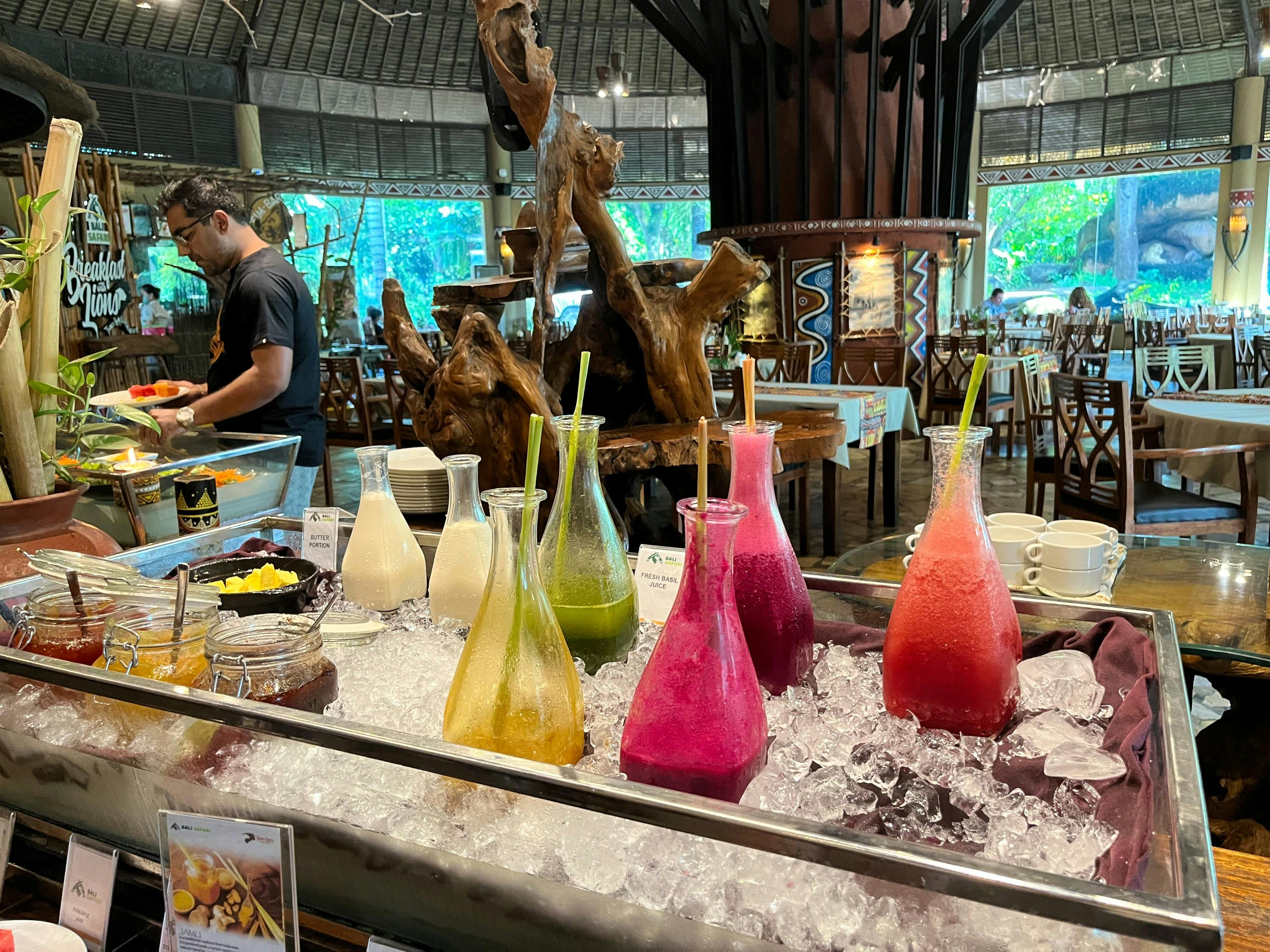 A counter displaying colorful juice bottles on ice in a restaurant with wooden decor and a staff member in the background.