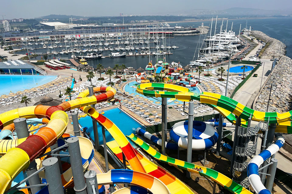 Water park with colorful slides and pools next to a marina filled with yachts and boats.