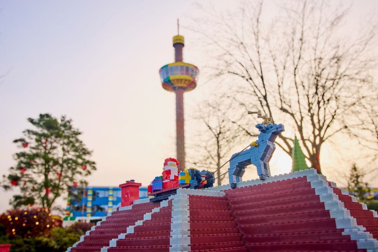Лего Санта и олени на крыше, с разноцветной смотровой башней и безлиственными деревьями на заднем плане.