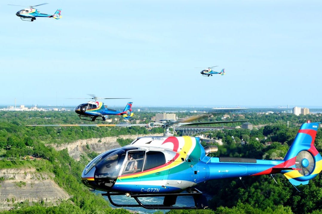 Three colorful helicopters flying over a green canyon with a city and bridge visible in the background.