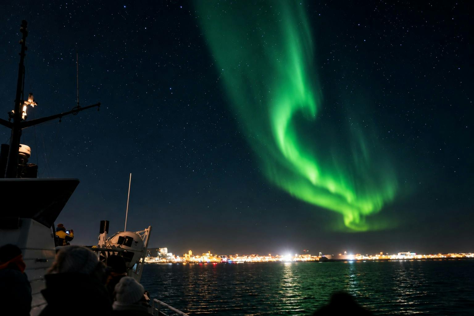 Green aurora borealis over a city skyline at night, viewed from a boat on the water with people observing.