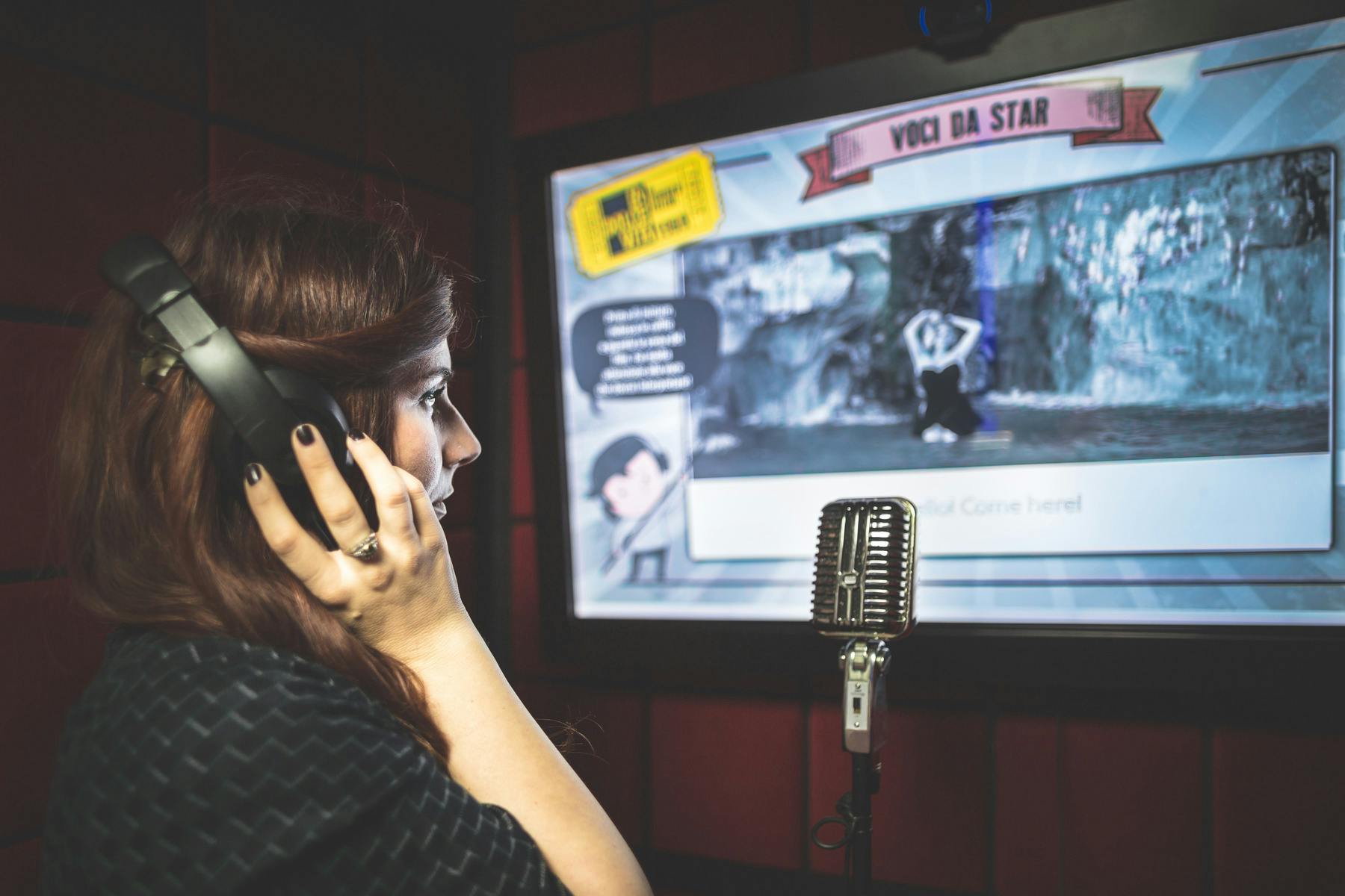 Una persona con gli auricolari canta in un microfono davanti a uno schermo su cui vengono visualizzati i testi e le immagini del karaoke.