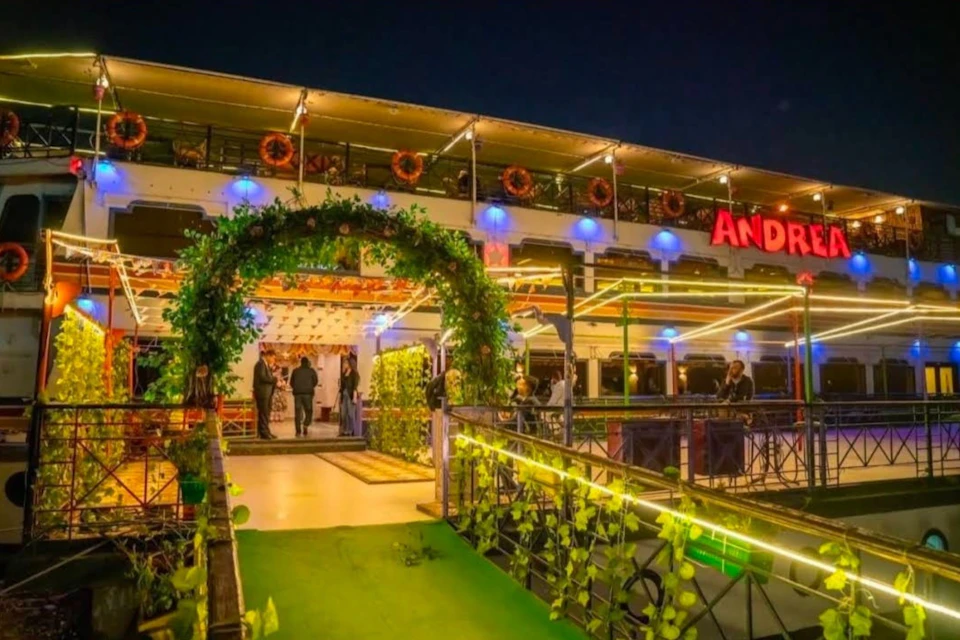 A brightly lit restaurant with an ornate entrance arch covered in greenery and a neon sign at night.