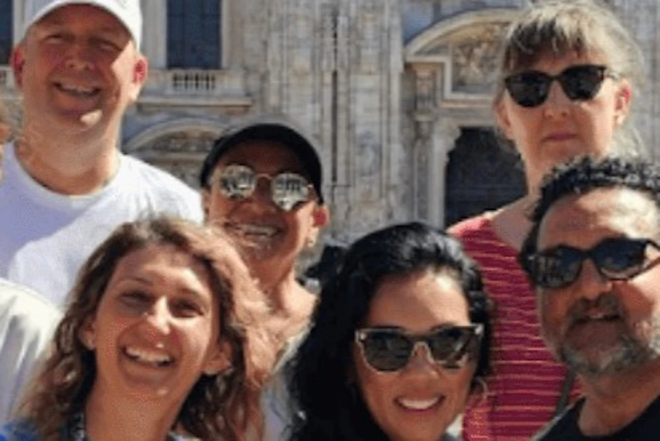 Group of people smiling in front of a large, ornate building with Gothic architecture and pointed arches.