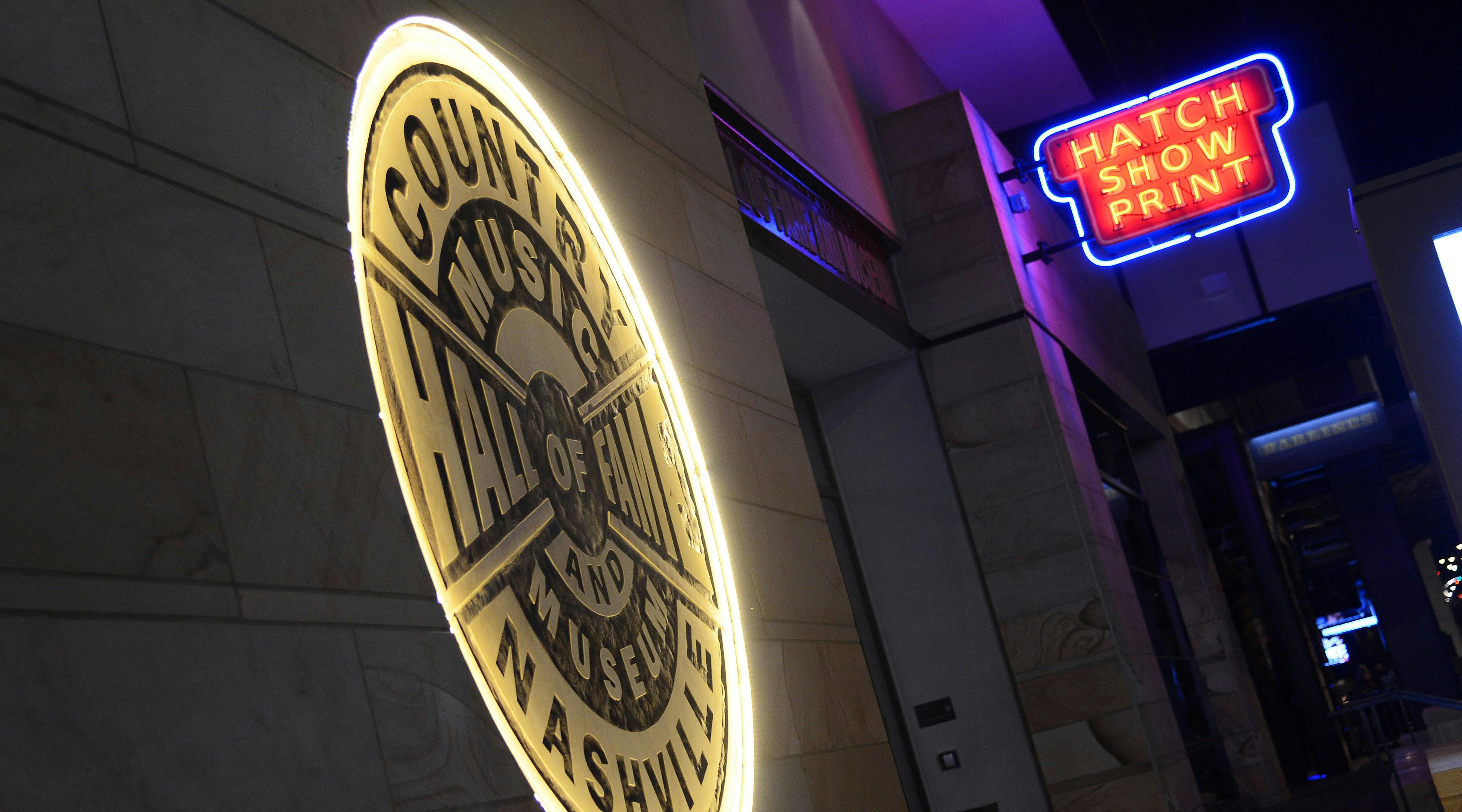 Illuminated sign reading "Country Music Hall of Fame and Museum Nashville" beside a blue and red neon sign for Hard Rock Cafe.