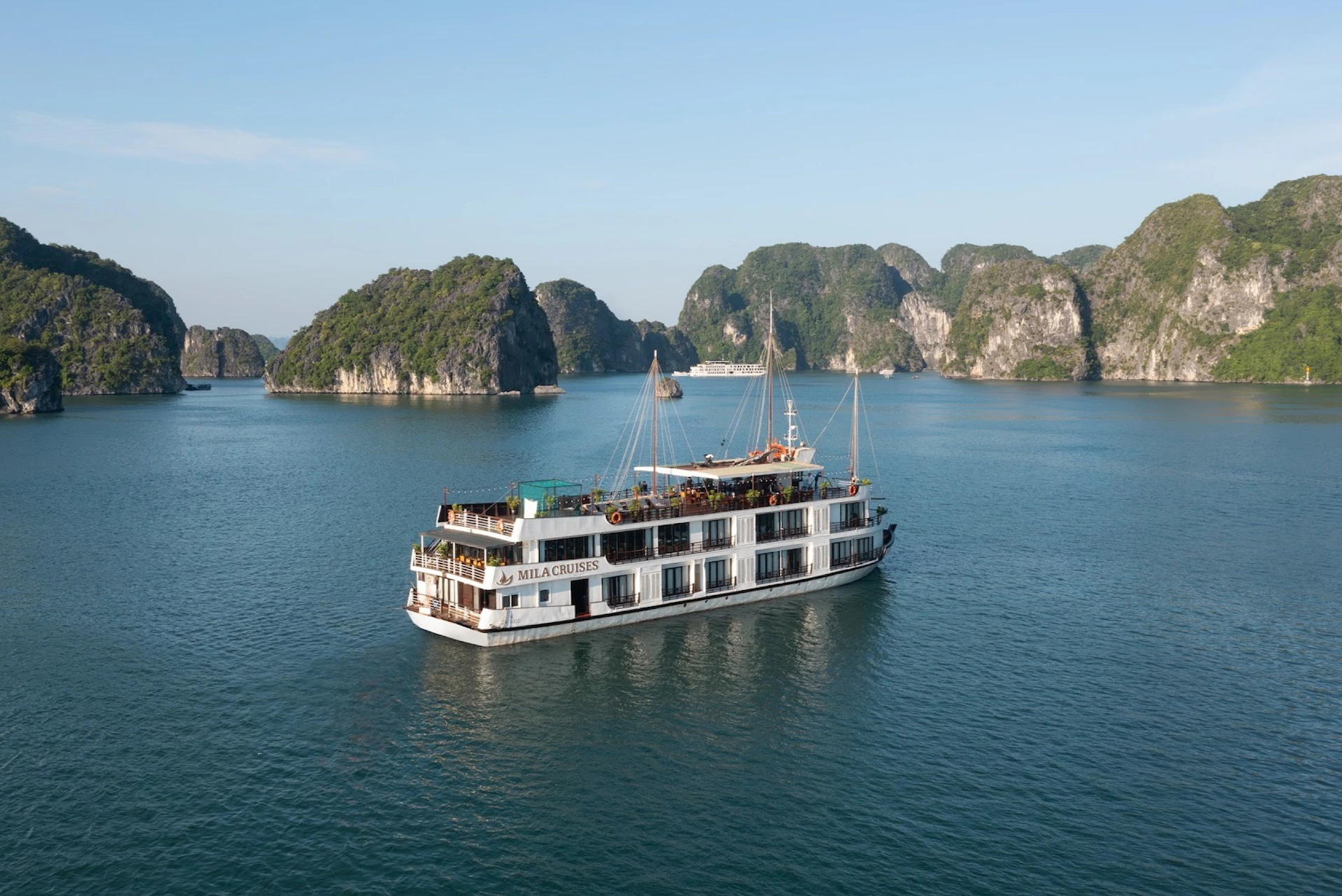 A cruise ship named "Milachistes" sails in calm waters with rocky, green islands in the background under a clear blue sky.