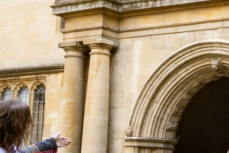 A guide showing a group of people an ornate historical building in a stone-paved courtyard.