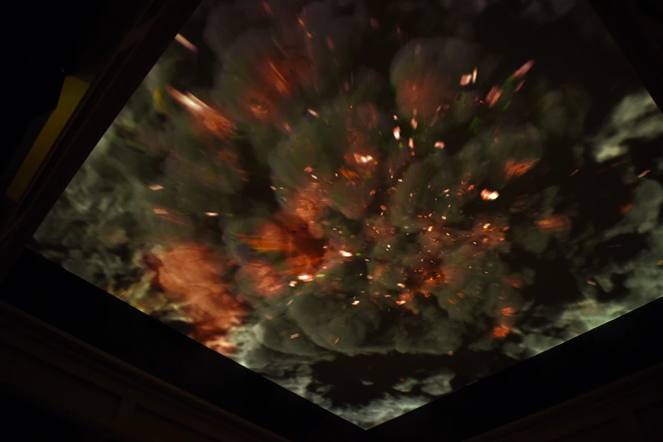 A dramatic depiction of an explosion with fiery and smoky effects on a large screen or ceiling display.