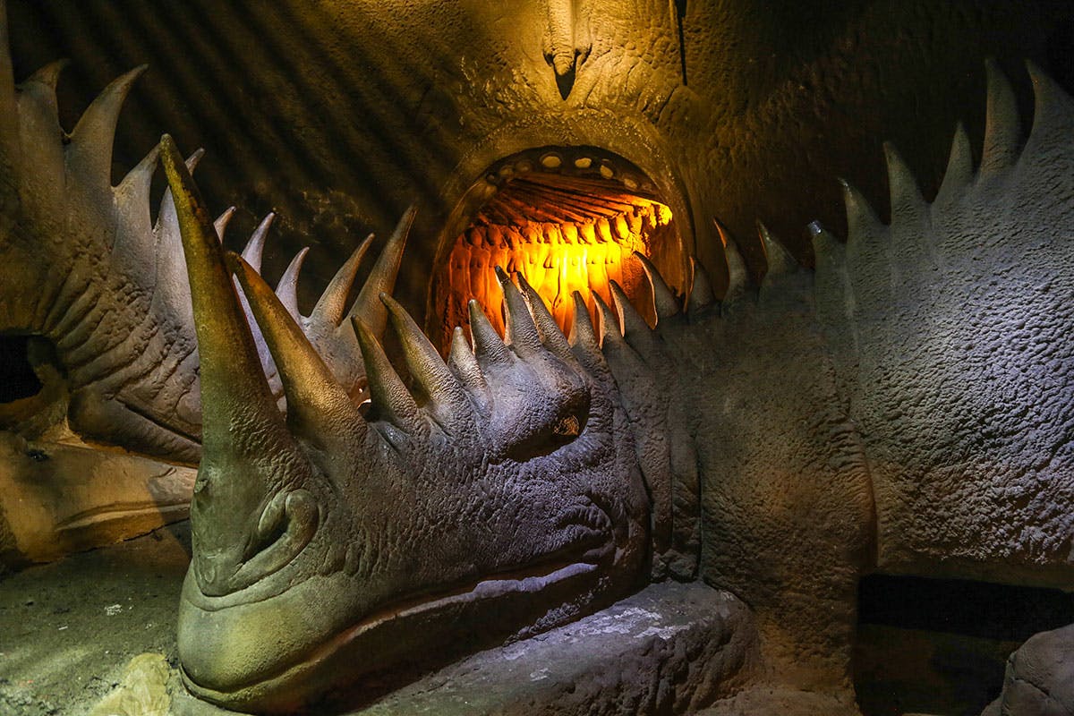 Ένα μεγάλο, πέτρινο γλυπτό ενός πλάσματος με εμφανείς αιχμές, υπό ζεστό φωτισμό, μέσα σε ένα σκοτεινό σκηνικό που μοιάζει με σπηλιά.