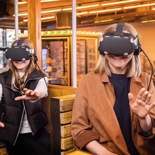 Tre personer bär VR-headset, sitter på träbänkar inomhus, ler och interagerar med den virtuella miljön.