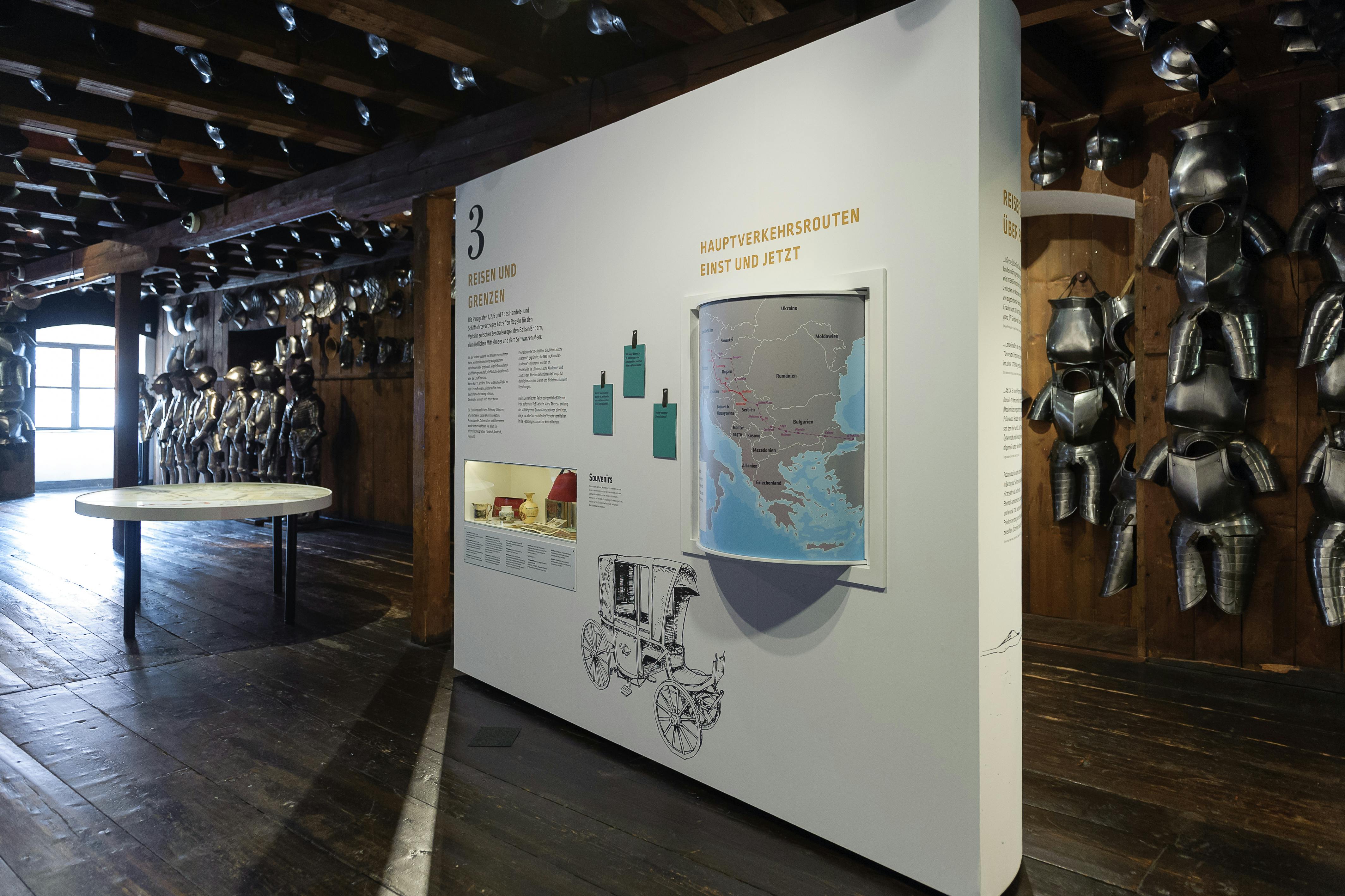 Exhibit with a map and text, showing historic travel routes. Suits of armor displayed in the background. Dark wooden flooring and ceiling.